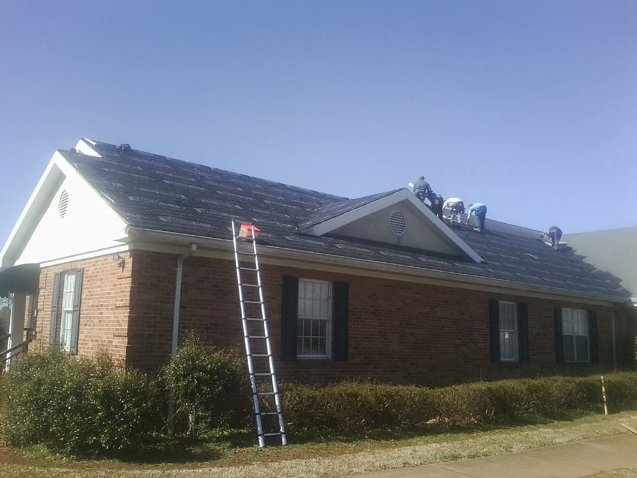 Crew tearing shingles off a brick ranch roof with a ladder set — Metal Roof Repair work by our crew in West Plains