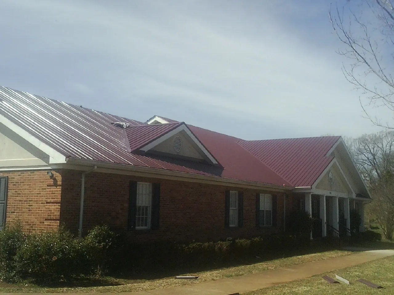 Red metal roof with gabled entries on a long brick building, from a Hail Damage Roof Repair job in West Plains