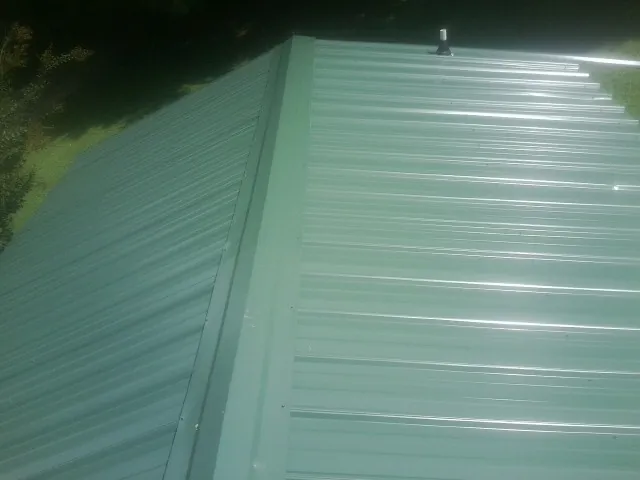New green metal panels meeting at the ridge of a roof — Flat Roof Repair work by our crew in West Plains