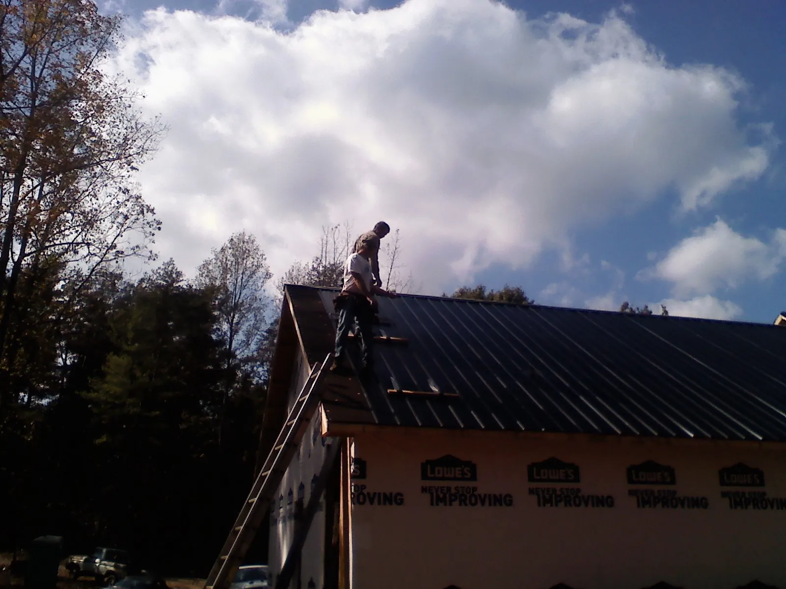 Roofer fastening dark metal panels high against a cloudy sky, from a Roof Inspection job in West Plains