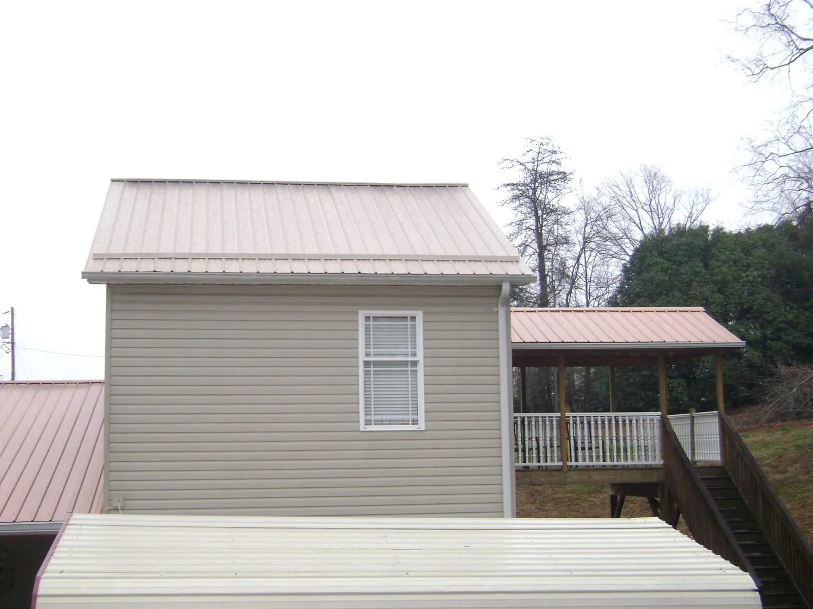 Tan metal roofs on a two story addition and attached porch, from a Roof Replacement job in West Plains